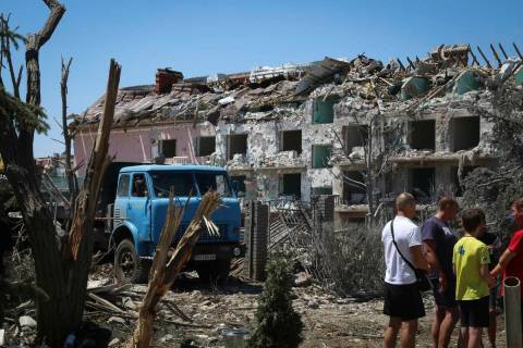 FILE - Local residents stand next to damaged residential building in the town of Serhiivka, loc ...