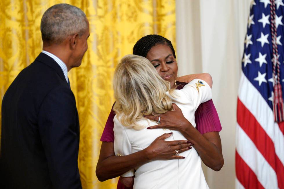 Former President Barack Obama looks on as former first lady Michelle Obama hugs first lady Jill ...