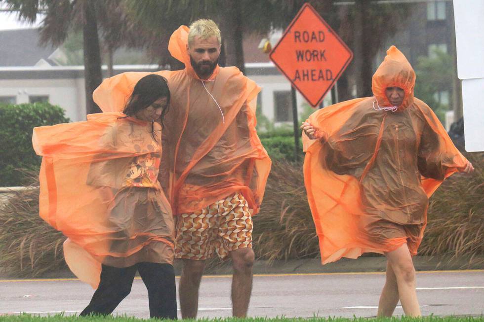 People in raincoats walk along International Drive in Orlando, Fla., Wednesday, Sept. 28, 2022, ...