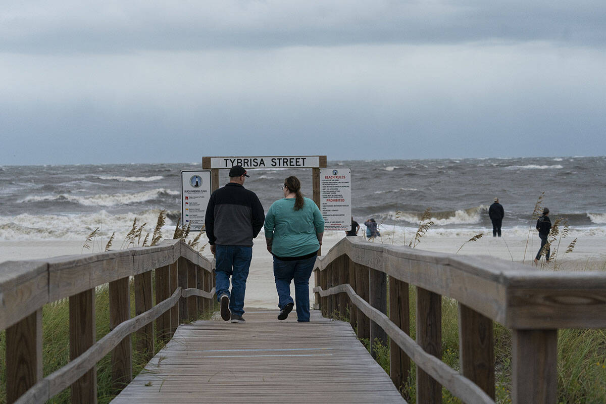People walk to look at the surf as the effects from Hurricane Ian are felt, Thursday, Sept. 29, ...