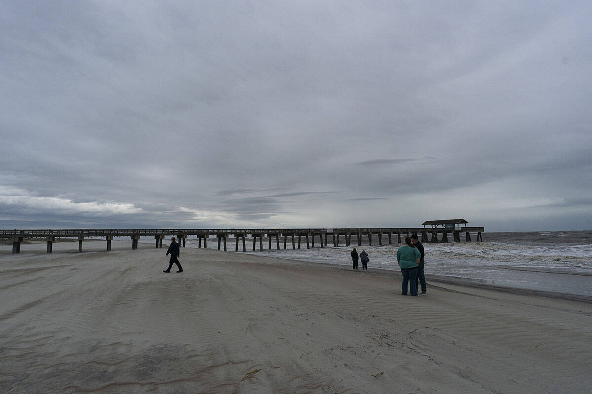 People walk near a pier as the effects from Hurricane Ian are felt, Thursday, Sept. 29, 2022, i ...