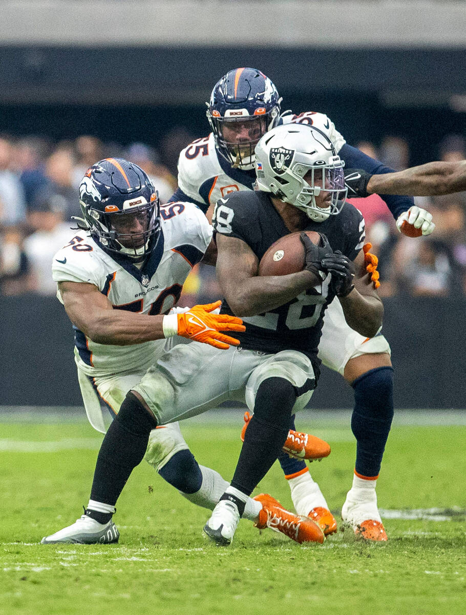 Raiders running back Josh Jacobs (28) tries to spin his way out of a tackle against Denver Bron ...