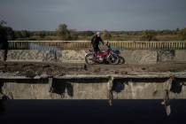 A man hauls his motorbike on a destroyed bridge across Oskil river during evacuation in recentl ...