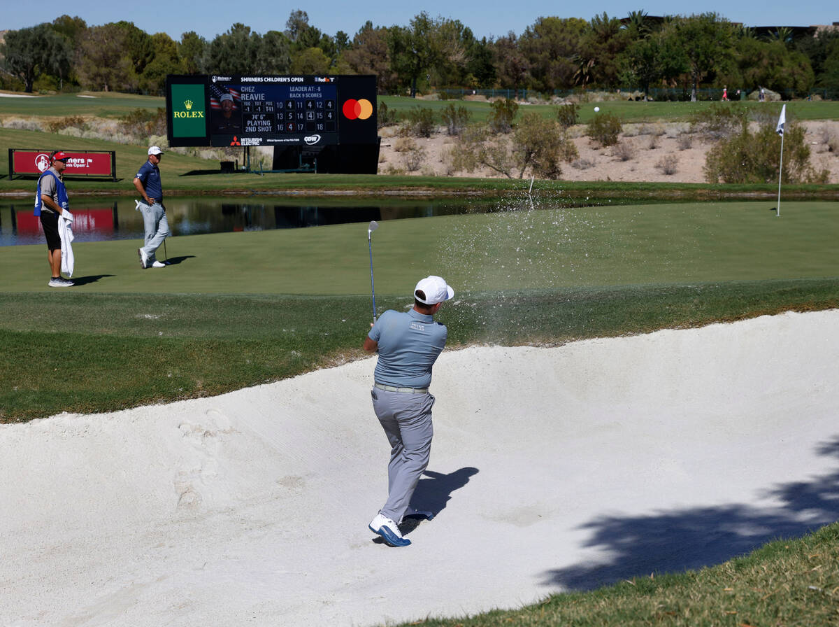 Chez Reavie hits out of the sand on the 17th green as Tom Hoge, left, looks on during the first ...