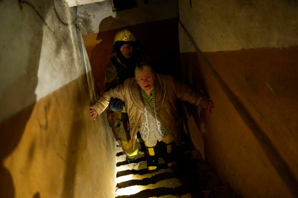 A woman is helped by a Ukrainian firefighter to leave a shelter after a Russian shelling in Kha ...