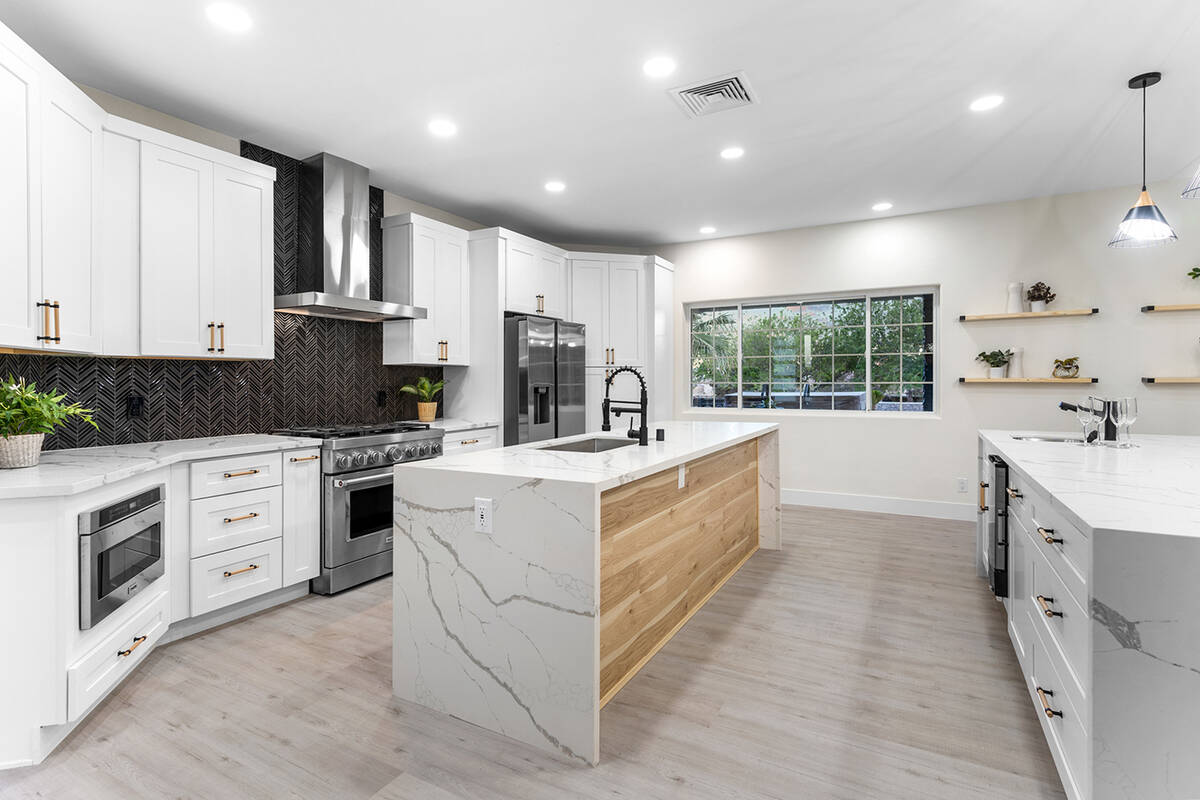 A black-and-white gourmet kitchen features dual waterfall islands with quartz countertops, stri ...