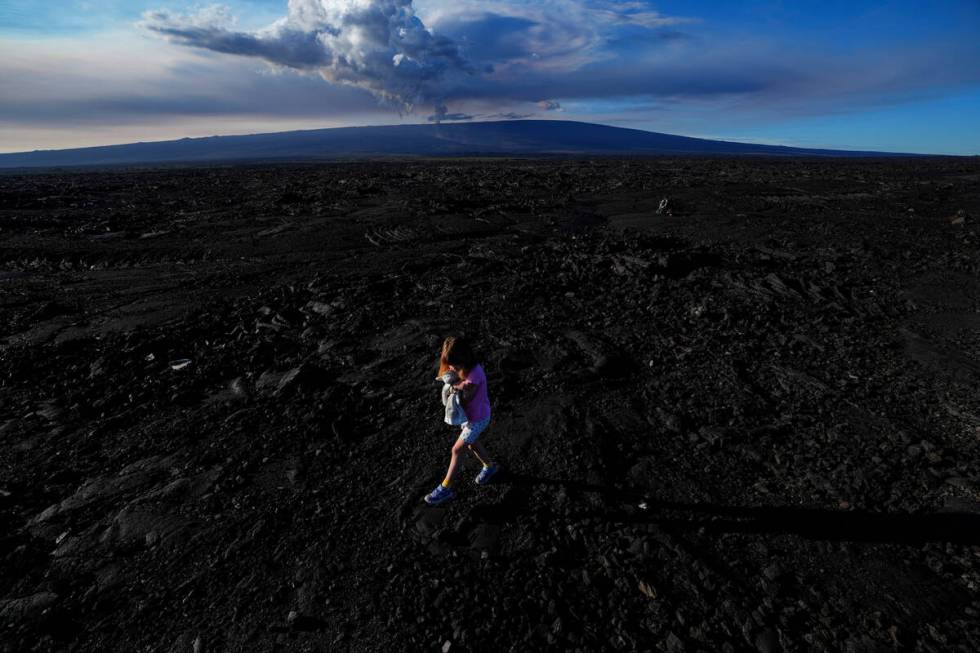 Abigail Dewar, of Alberta, Canada, holds a stuffed animal as she walks over hardened lava rock ...