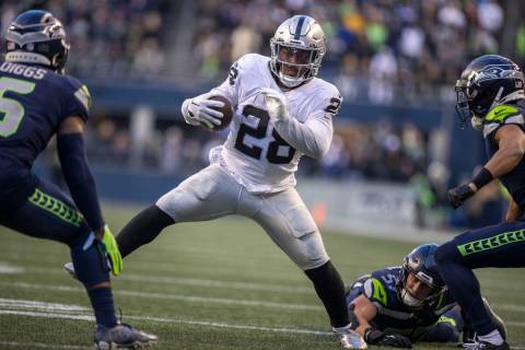 Raiders running back Josh Jacobs (28) looks for room to run with Seattle Seahawks safety Quandr ...