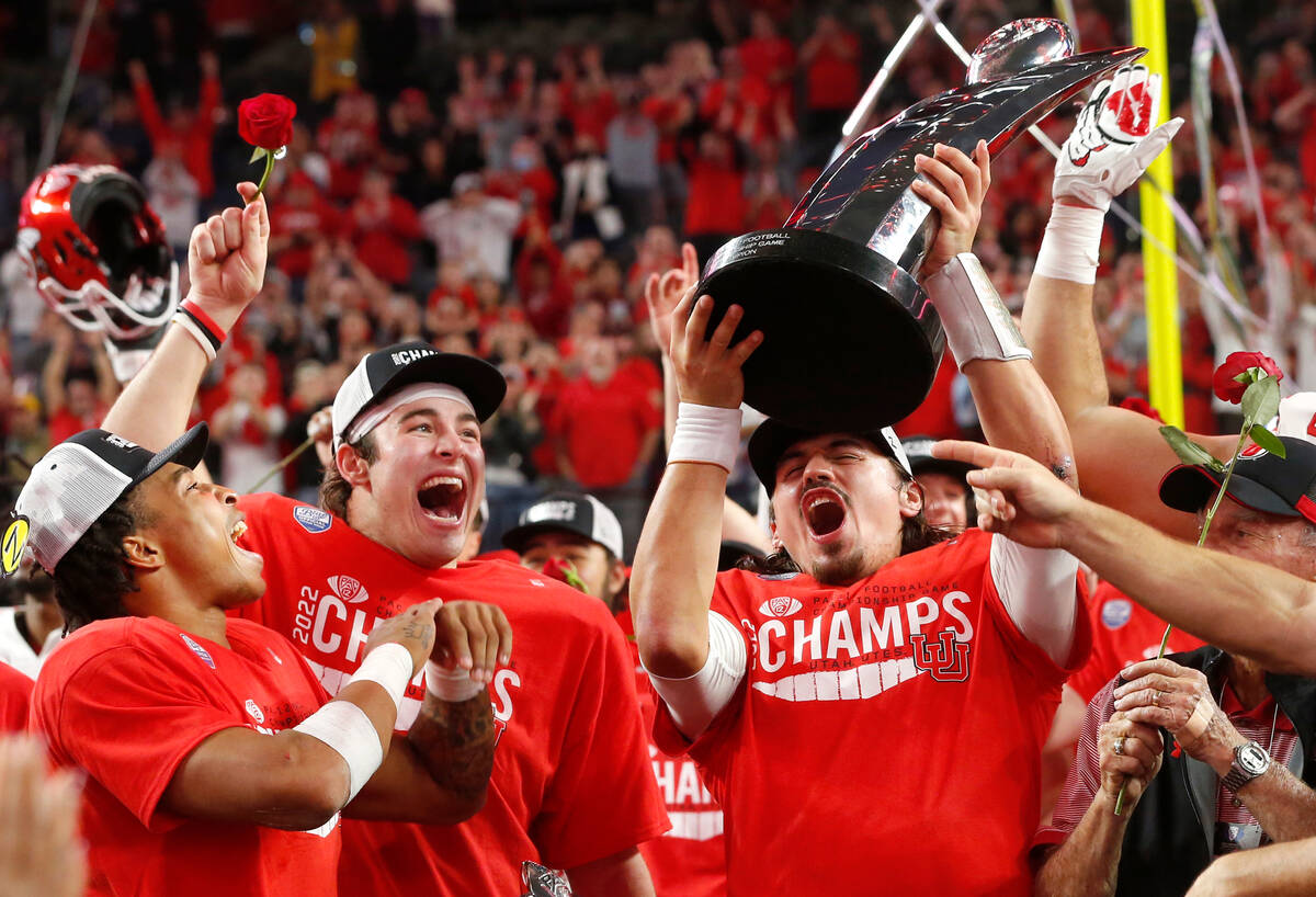 Utah quarterback Cameron Rising, right, holds up the trophy and celebrates with Dalton Kincaid, ...
