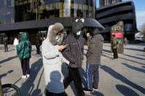 Residents wearing masks walk past others in line for COVID tests in Beijing, Wednesday, Dec. 7, ...