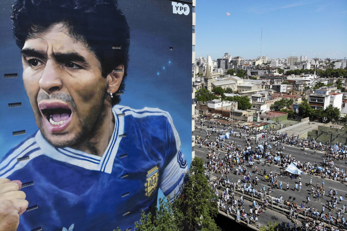 A mural of the late, soccer legend Diego Maradona stands tall as soccer fans walk to catch a gl ...