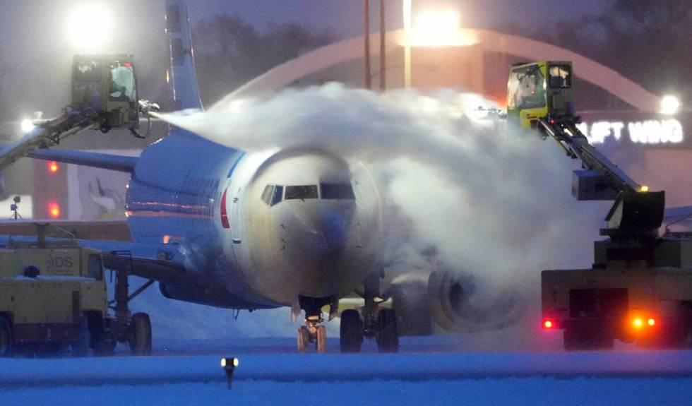 An American Airlines plane is de-iced as high winds whip around 7.5 inches of new snow at Minne ...