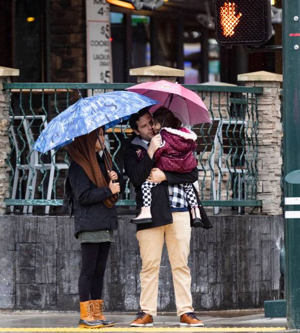 Pedestrians hold umbrellas to protect themselves from rain as they cross Fremont Street during ...