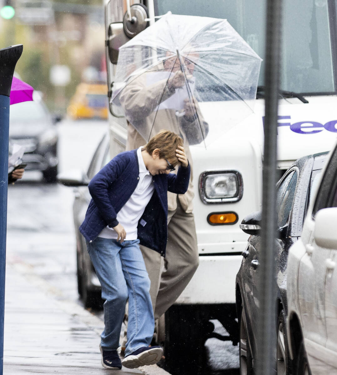 A man holds un umbrella to protect himself and a young boy from rain as they walk along Lewis A ...