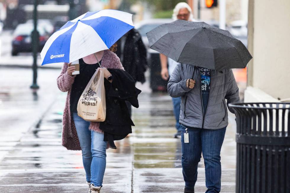 Pedestrians hold umbrellas to protect themselves from rain as they walk along Lewis Avenue duri ...