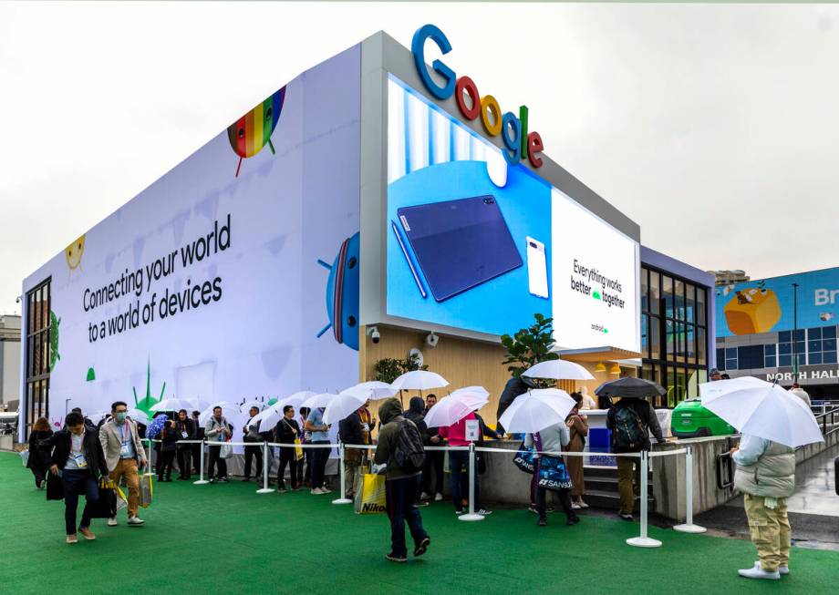 Attendees stay dry from the rain under umbrellas outside the Google display space during the op ...