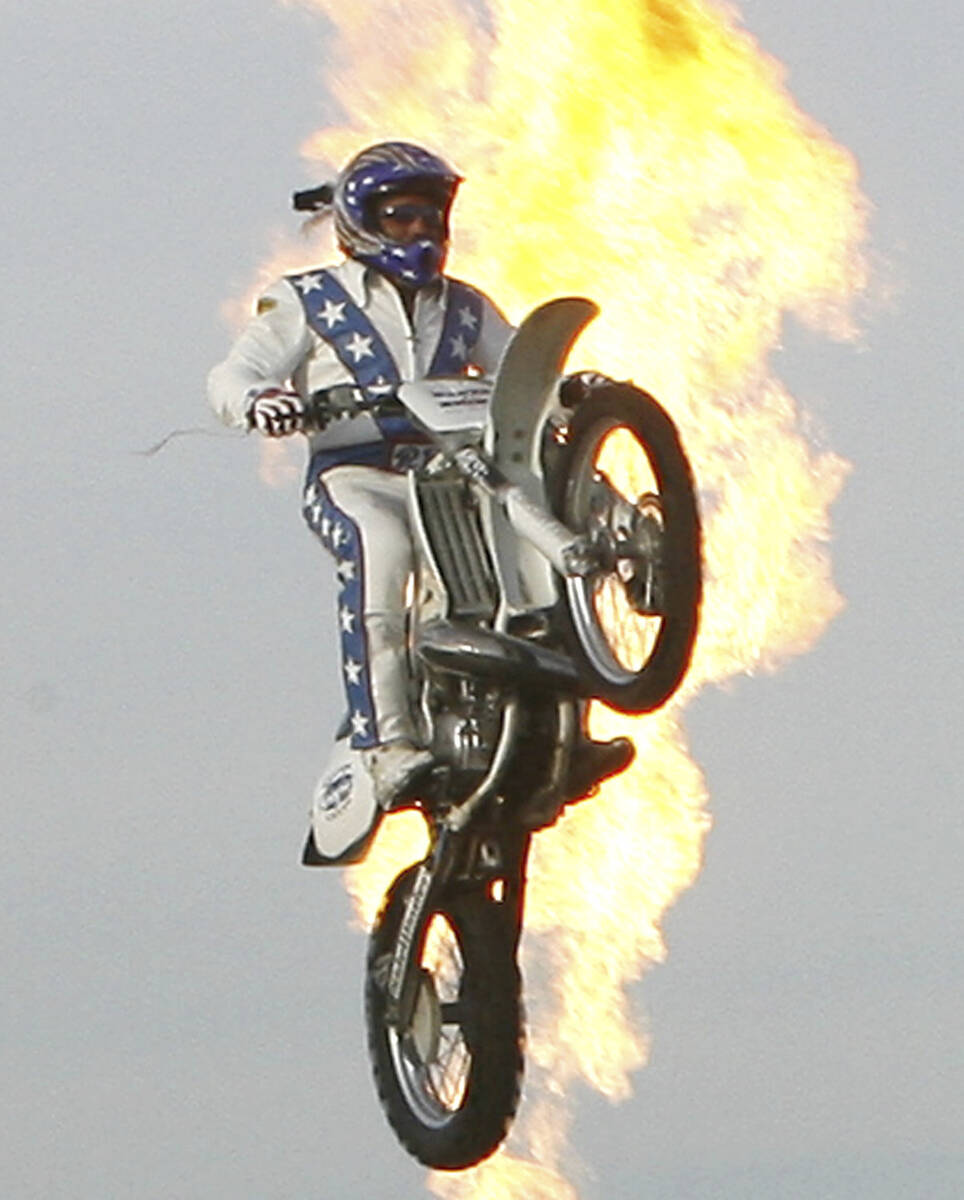 Robbie Knievel is backlit in flames as he jumps over 24 delivery trucks, a 200 foot gap, at Kin ...