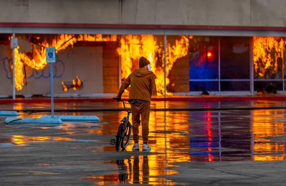 A masked bicycle rider looks on close by as Las Vegas and Clark County Firefighters work a full ...
