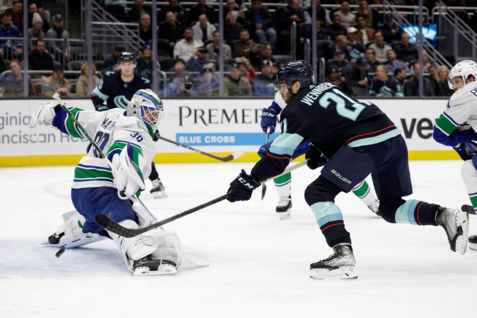 Seattle Kraken center Alex Wennberg (21) sends the puck past Vancouver Canucks goaltender Spenc ...