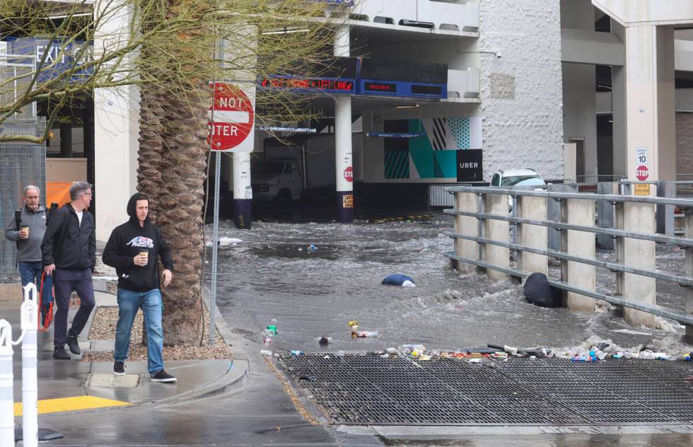 Pedestrians walk by as water flows from The Linq parking garage to a flood channel after rain o ...