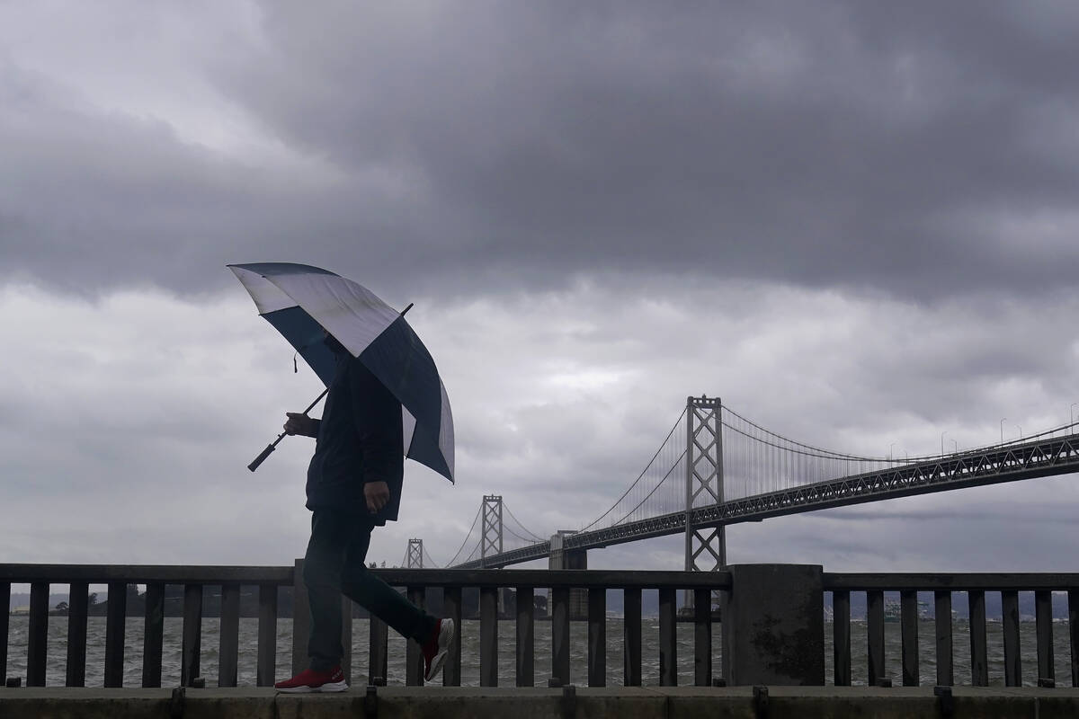 A pedestrian carries an umbrella while walking in front of the San Francisco-Oakland Bay Bridge ...