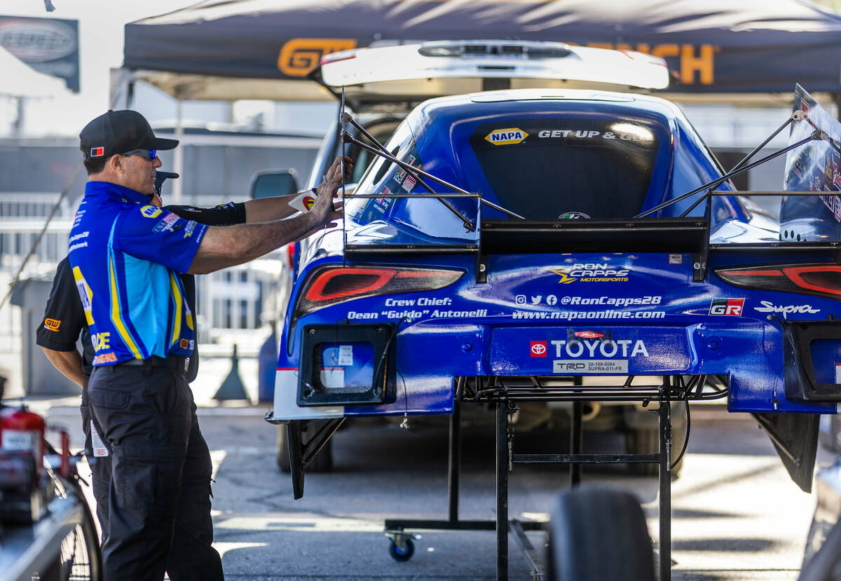 Funny Car driver Ron Capps looks to place a sticker on the side of his car in the pits during D ...