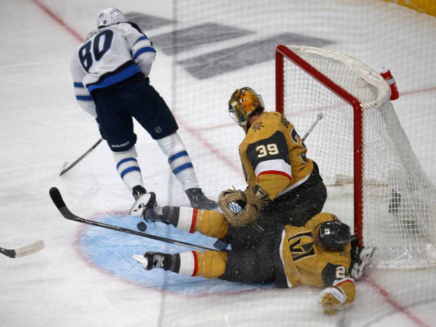 Golden Knights goaltender Laurent Brossoit (39) falls on Golden Knights defenseman Alec Martin ...