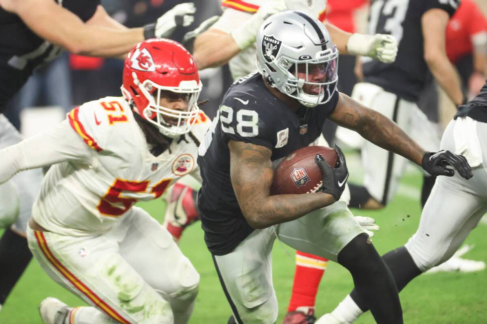 Raiders running back Josh Jacobs (28) runs the ball under pressure from Kansas City Chiefs defe ...