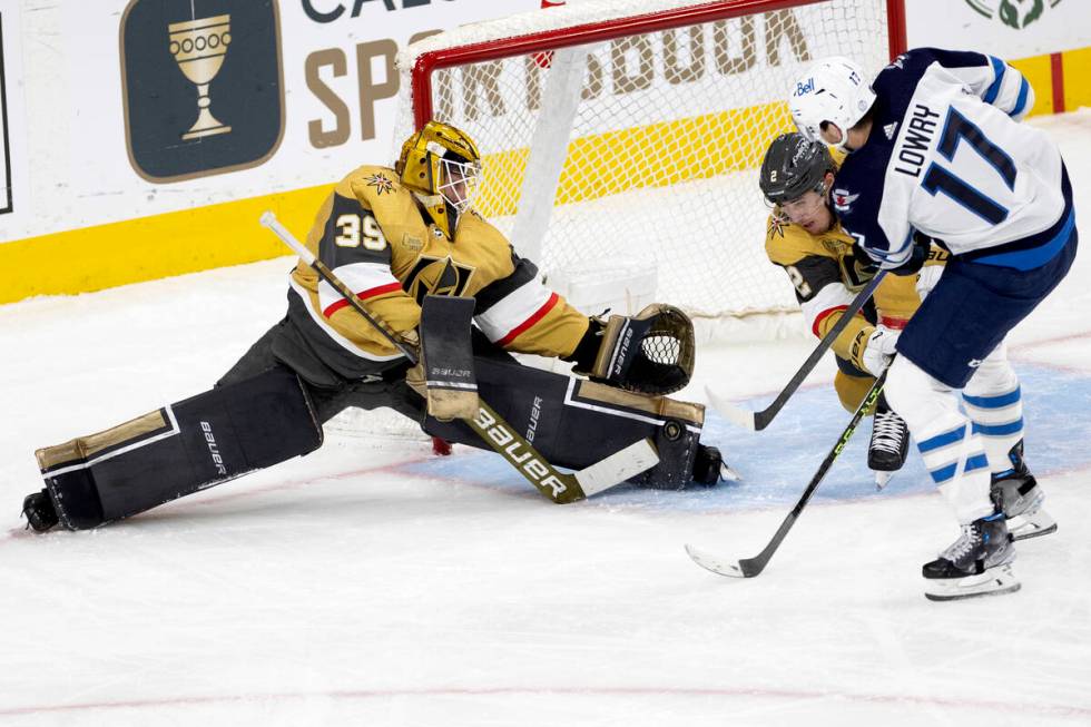 Golden Knights goaltender Laurent Brossoit (39) saves the puck while Winnipeg Jets center Adam ...