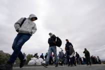 A group of migrants line up as they wait to apply for asylum after crossing the border, Wednesd ...