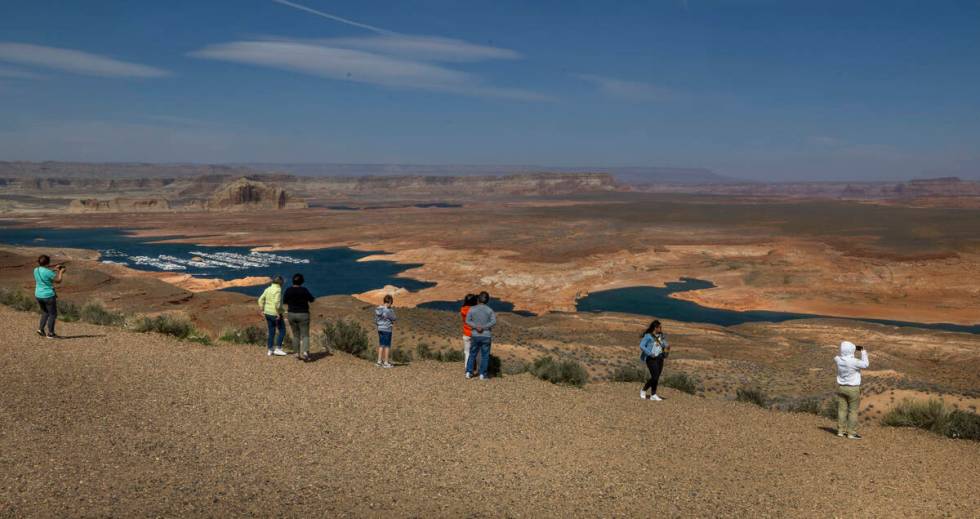 Visitors stand above and look at the declining expanse of Lake Powell as it feeds into the Colo ...