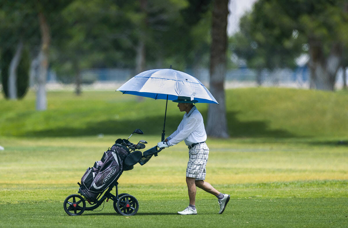 A golfer stays cool beneath an umbrella on the course at the Las Vegas Golf Club as hot weather ...