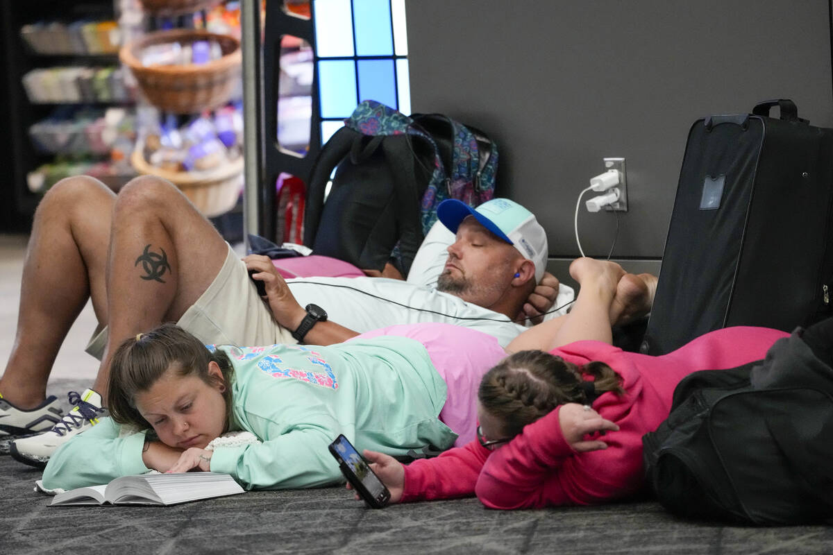 Travelers use their electronic devices while lying on the floor of the departures area of Termi ...
