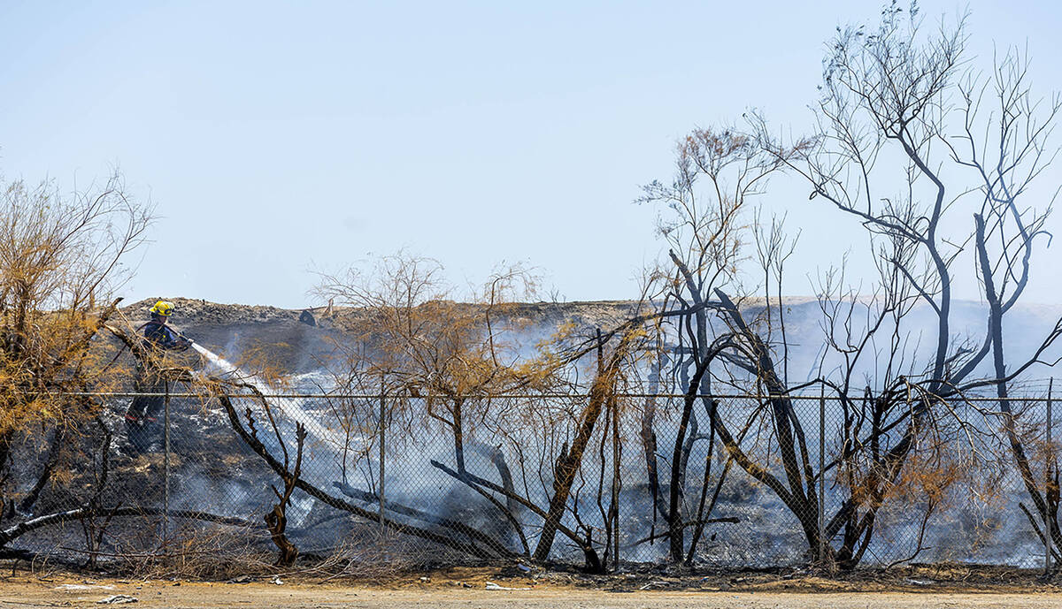 Clark County firefighters extinguish a brush fire adjacent to the Las Vegas Wash along the far ...