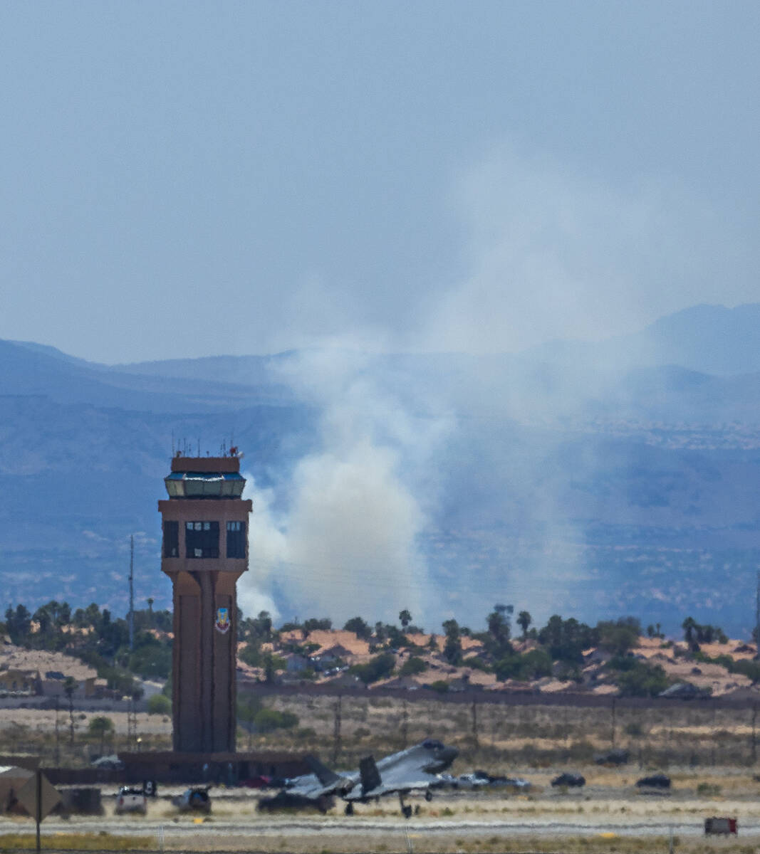 A fighter jet lands at Nellis Air Force Base as smoke from a brush fire rises adjacent to the L ...