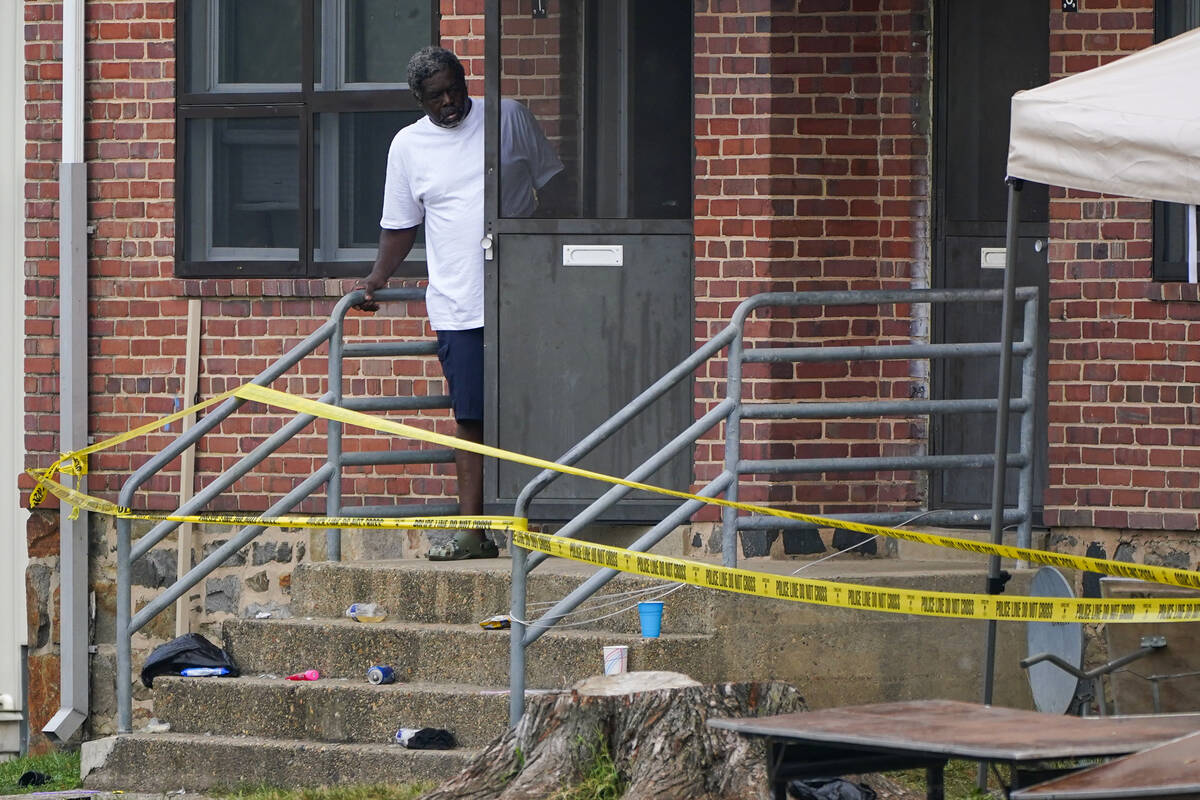 A person looks out the front door of a home as police tape surrounds the area of a mass shootin ...