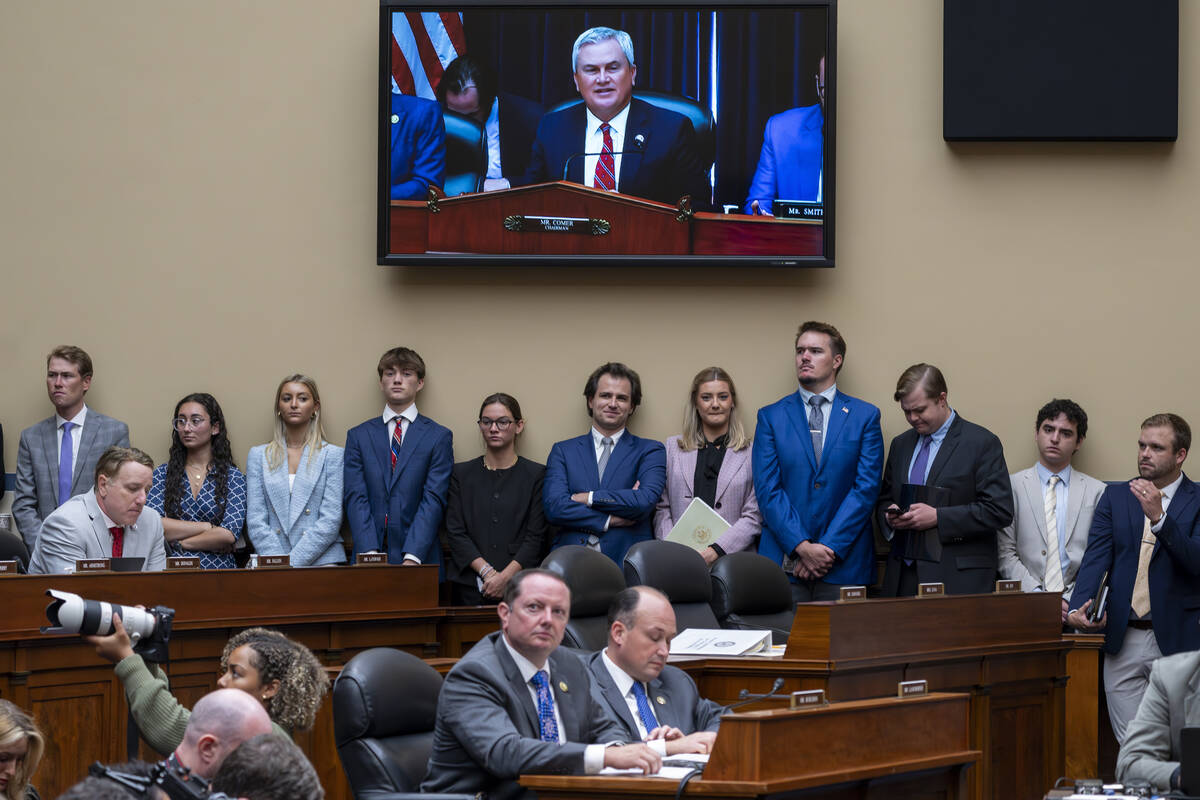 Congressional staffers stand beneath a monitor showing House Oversight and Accountability Commi ...