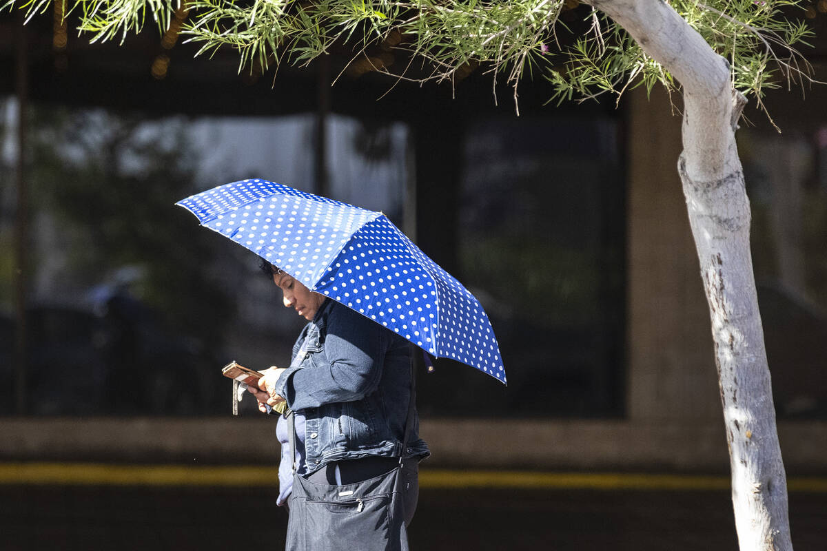 A woman holds an umbrella to protect herself from sun as she walks along Ogden Avenue in downto ...