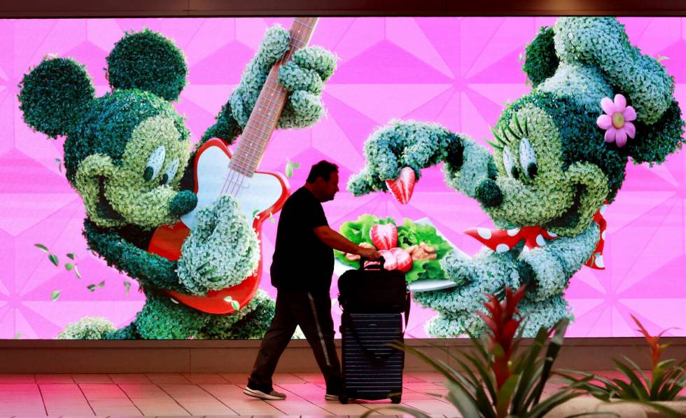 A traveler walks past a jumbo screen projecting images of Walt Disney World in the east hall at ...