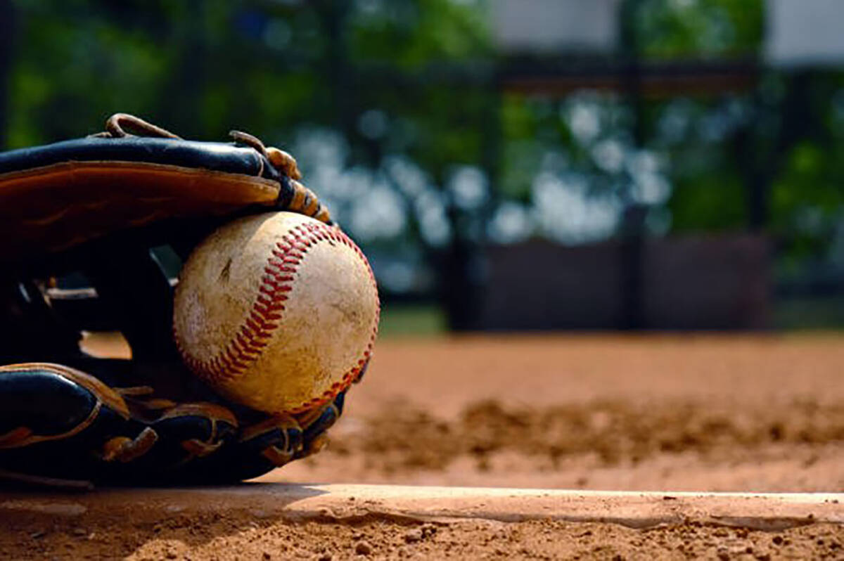 Baseball in glove laying on pitcher's mound of ball field.