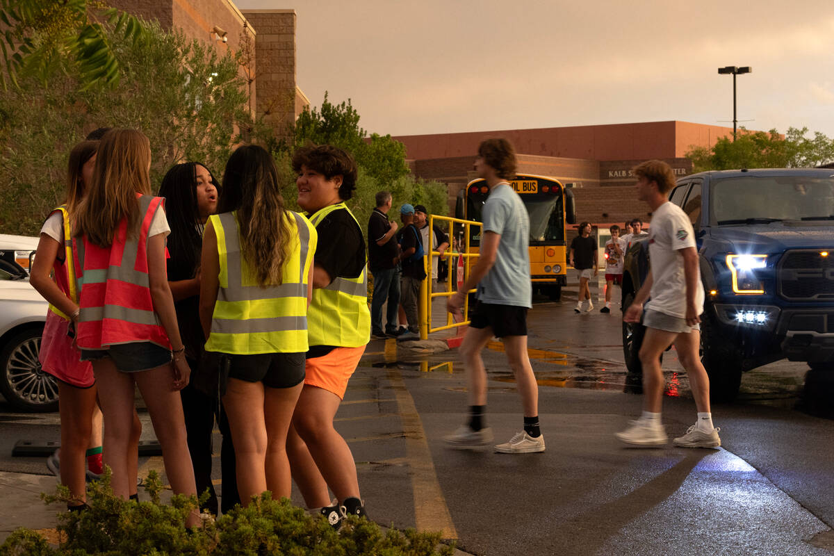 Students linger outside the football field as they wait for rain and lightning to clear before ...