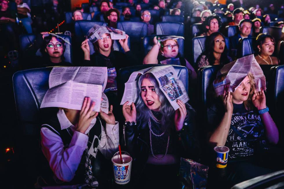 Audience members cover their heads with newspapers to shield themselves from imaginary rain dur ...