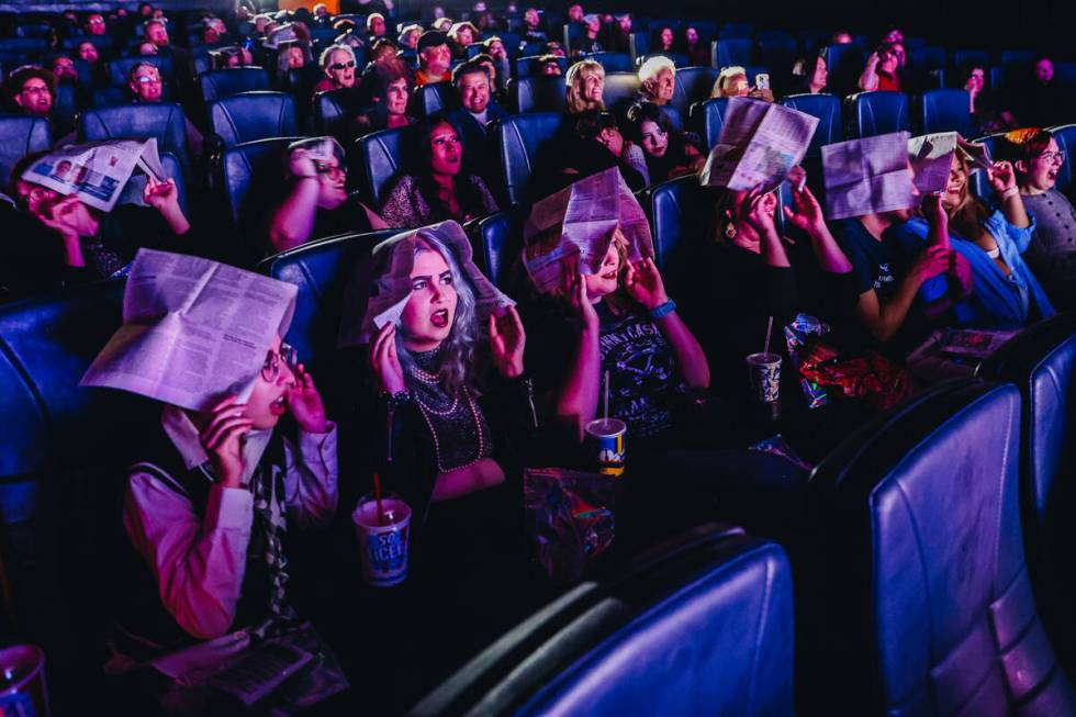 Audience members cover their heads with newspapers to shield themselves from imaginary rain dur ...