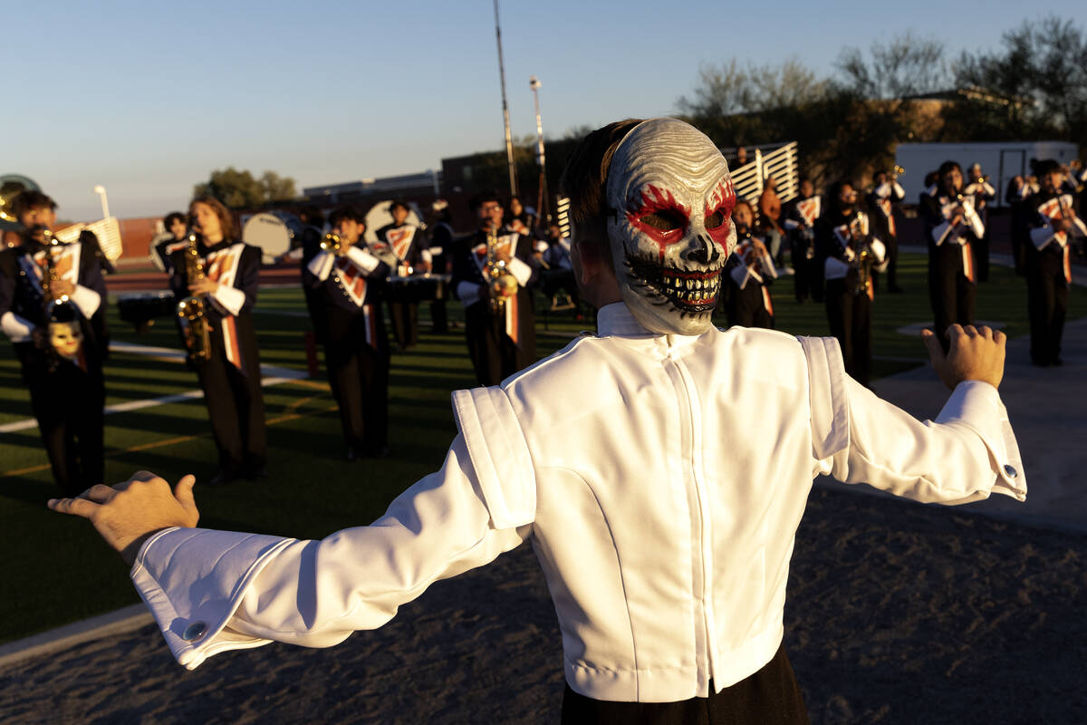A Legacy drum major conducts the band while wearing a spooky mask before a high school football ...