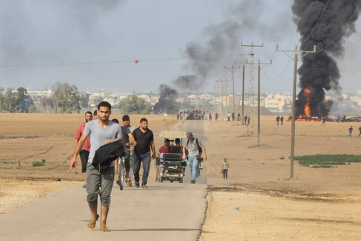 Palestinians walk away from the kibbutz of Kfar Azza, Israel, near the fence with the Gaza stri ...