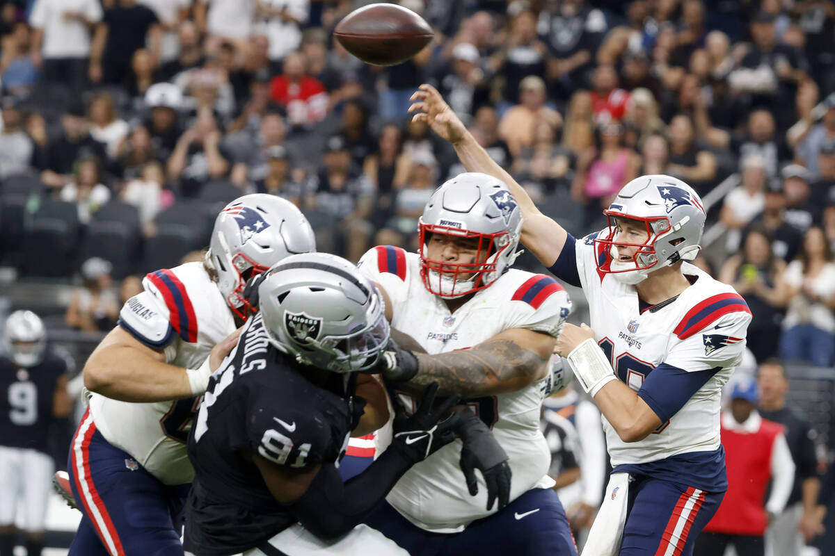 New England Patriots quarterback Mac Jones (10) throws under pressure from Raiders defensive ta ...