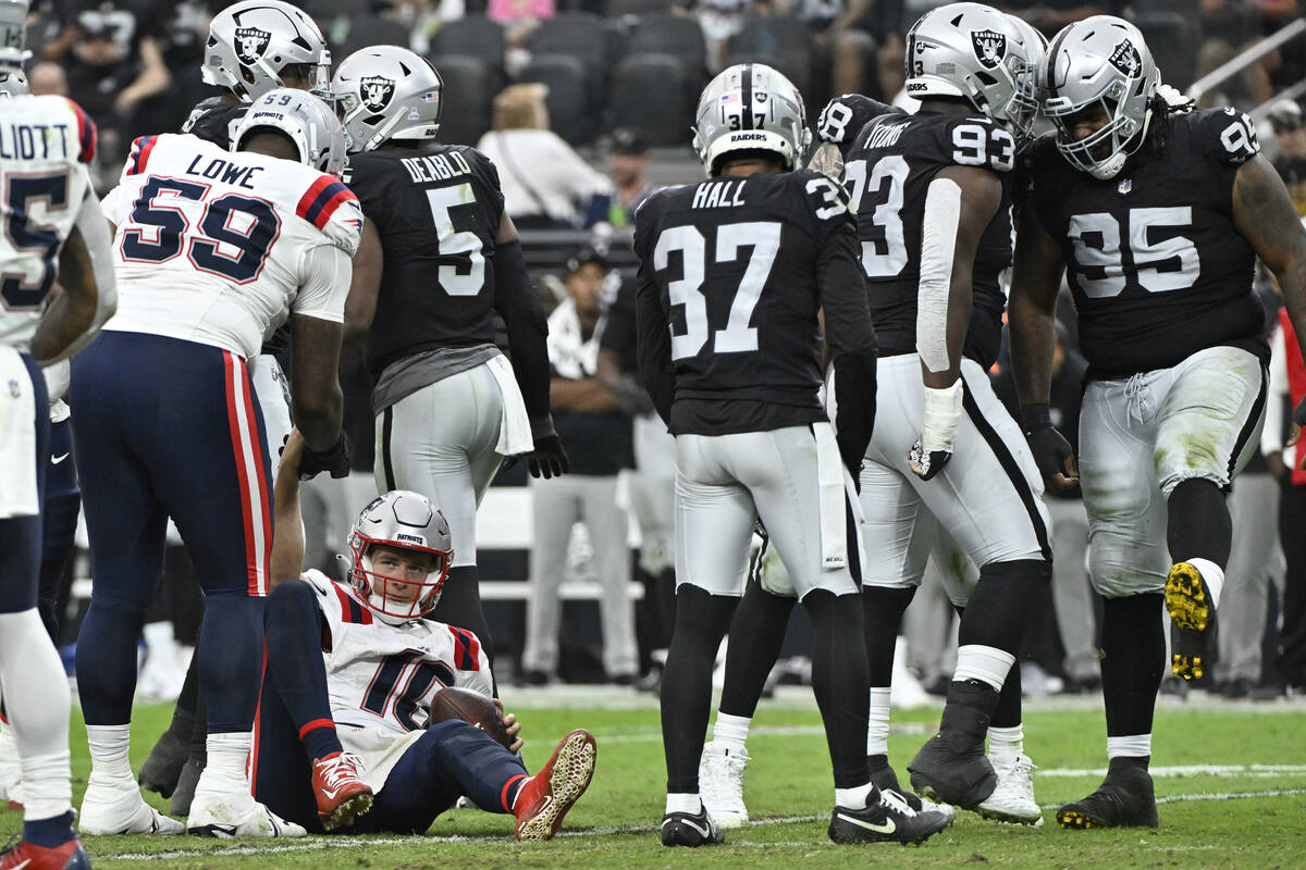 New England Patriots quarterback Mac Jones, below left, is helped up after being sacked by Las ...