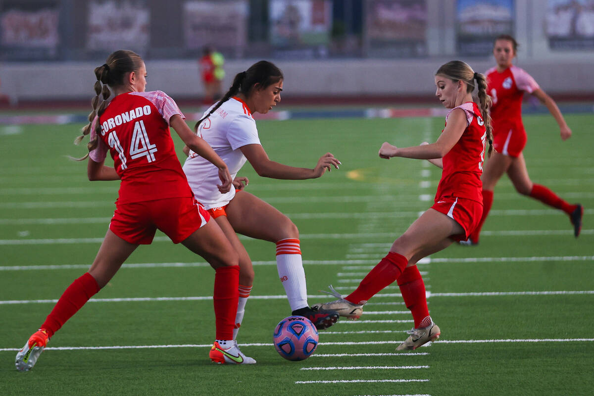 A Bishop Gorman player attempts to move the ball around two Coronado players during a soccer ga ...