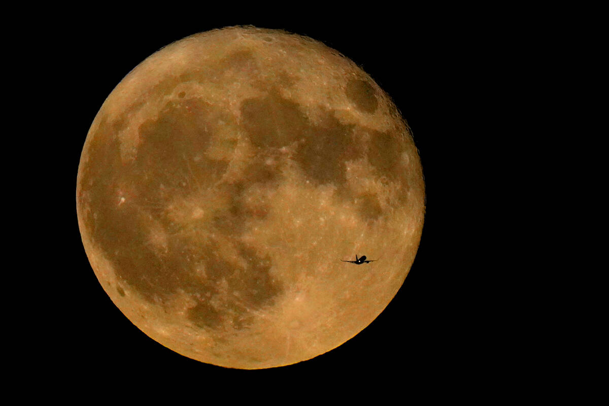 A commercial airliner flies across Lake Michigan in front of the "Full Buck" supermoon, the fir ...