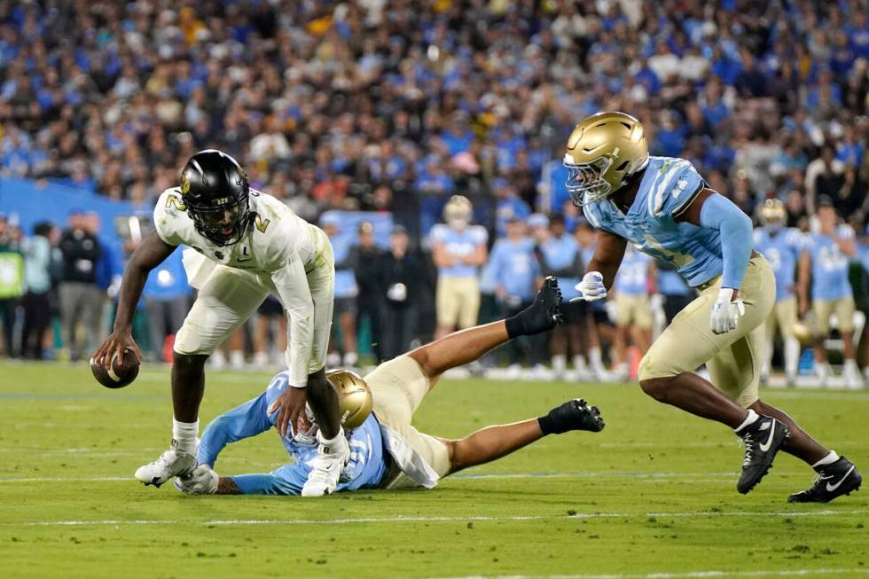 Colorado quarterback Shedeur Sanders, left, is tripped up by UCLA defensive lineman Laiatu Latu ...